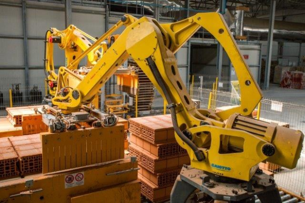 Großes Industrie-Lager mit gestapelten Kisten, Kränen, Zaun, Pfählen und einer fernen Wand in einer automatisierten Fertigungsumgebung.