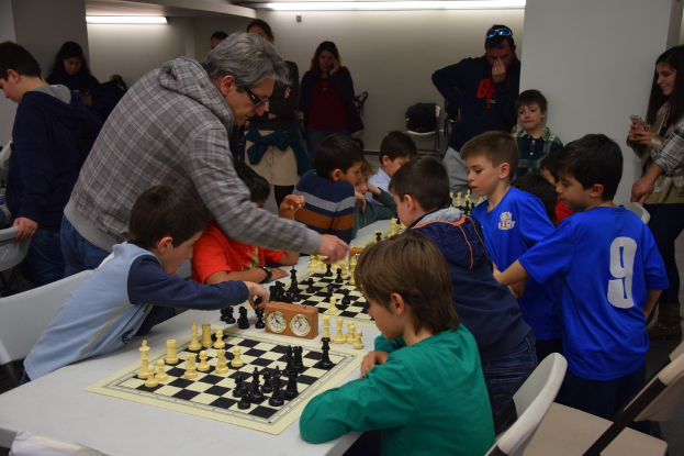 Kinder beim Schachspielen in einem Wettbewerb, der von Erwachsenen im Hintergrund beobachtet wird.