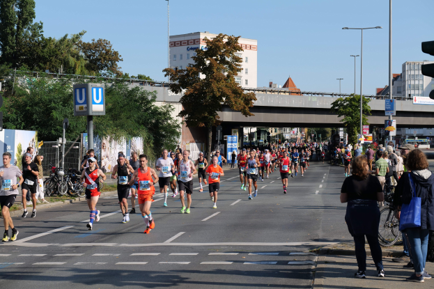 Gruppe von Läufern bei einem Marathon auf einer baumgesäumten Straße unter einem klaren blauen Himmel.