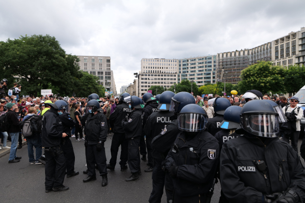 Eine große Gruppe von Polizisten steht vor einer Menschenmenge auf einer Straße mit Bäumen und Gebäuden unter einem bewölkten Himmel während einer Demonstration in Berlin, Deutschland.