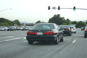 Eine vielbefahrene Straße mit mehreren Fahrzeugen, drei Strommasten und einer Ampel auf der rechten Seite unter einem klaren Himmel.