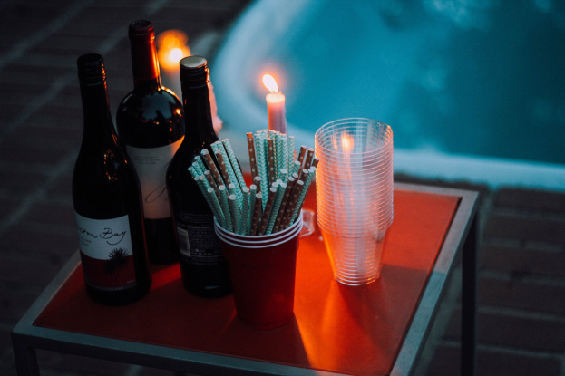 Zwei Flaschen Wein, eine Kerze, Gläser und Strohhalme auf einem Tisch neben einem Swimmingpool.