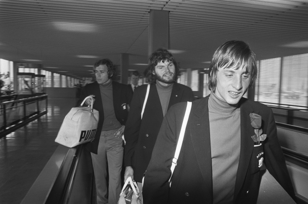 Eine Gruppe von Männern in Schwarz und Weiß auf einer Rolltreppe in einem Flughafen, jeder trägt eine Tasche.