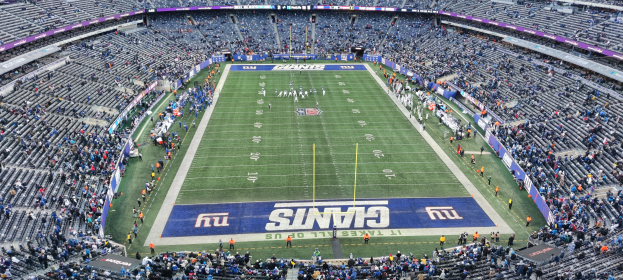 Ein Fußballstadion voller Zuschauer, Spieler, Pfosten und Tafeln mit Text, alles in Reihen von Stühlen sitzend.