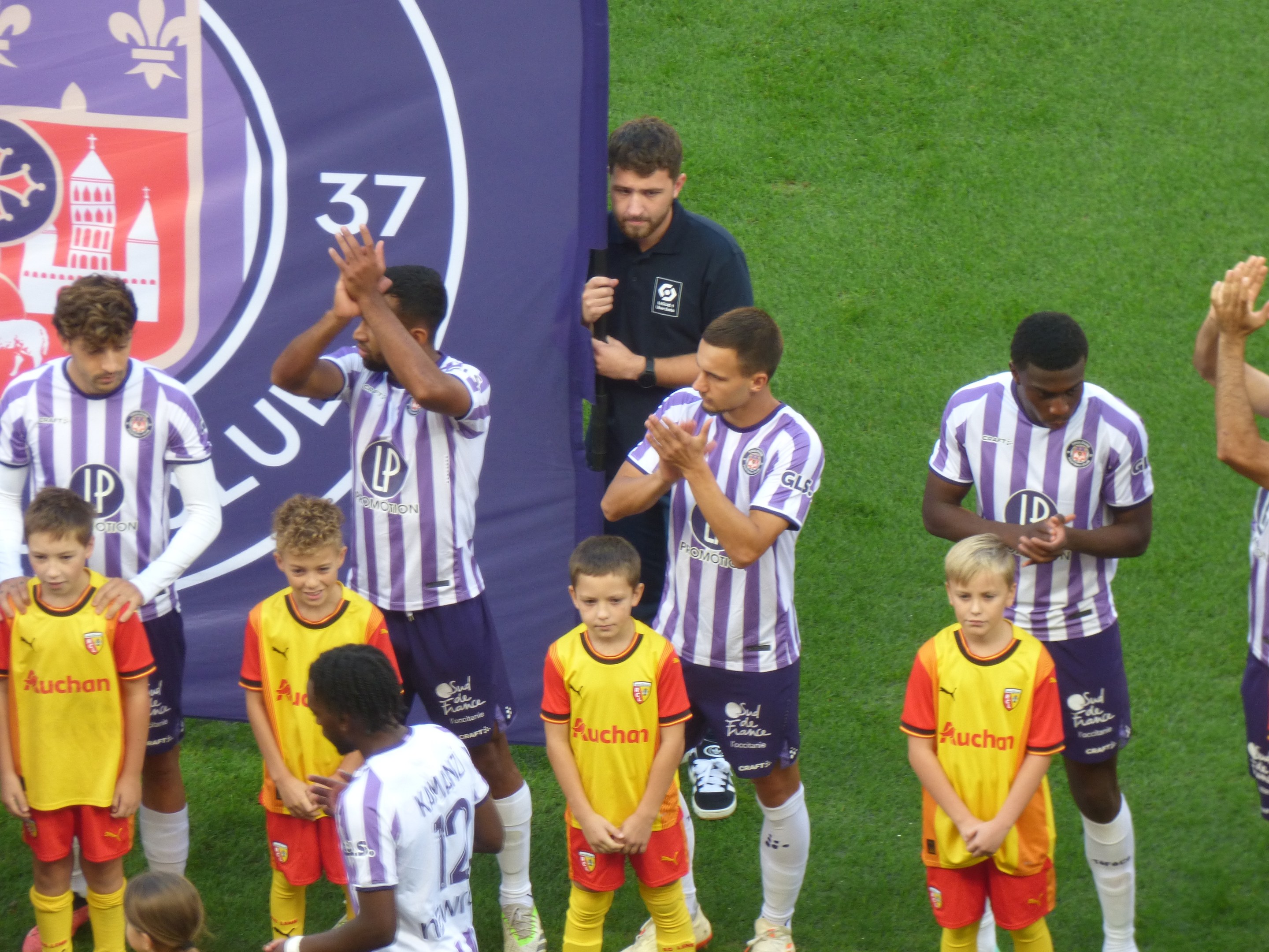 Eine Gruppe junger Jungs auf einem Fußballfeld, die klatschen, mit einem Banner im Hintergrund mit Text und Logos.