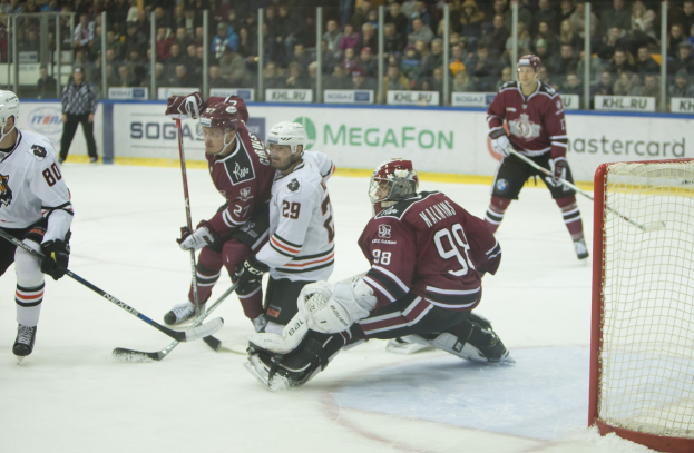 Eine Gruppe von Menschen, die Hockey auf einem Eisstadion mit Torpfosten spielen, umgeben von Zuschauern in Tribünen und Bannern im Hintergrund.