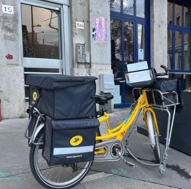 Ein gelbes Fahrrad mit mehreren Taschen am Gepäckträger steht vor einem Gebäude mit Glastüren und Fenstern.