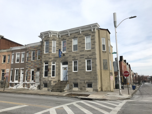 Eine Reihe neuer Häuser an einer Straßenecke in Philadelphia, mit Fenstern, Türen, Geländern, Laternen, Schildern und Fahrzeugen, sowie Bäumen und einem bewölkten Himmel im Hintergrund.