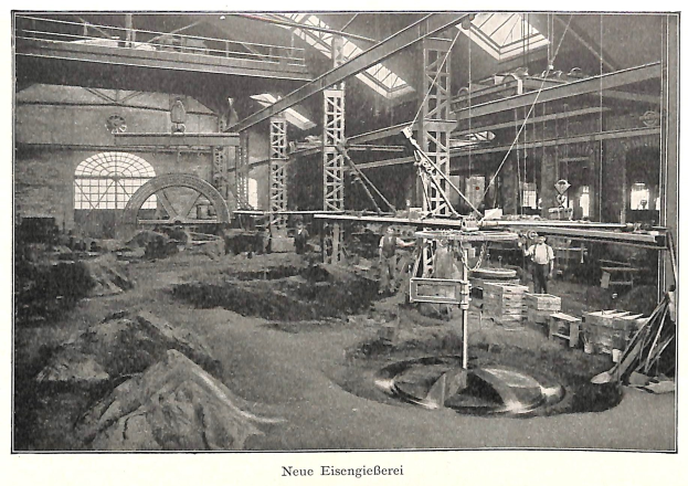 Schwarze und weiße Fotografie eines Fabrikinneren mit Arbeitern, die Maschinen bedienen, umgeben von Metallstangen und -pfählen, beschriftet mit "Neue Eisenglebeerei, die erste Fabrik Deutschlands" unten.