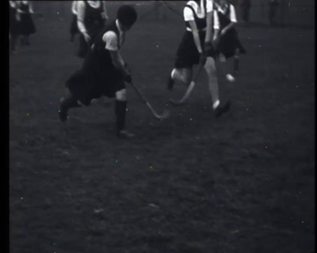 Schwarzes und weißes Foto einer Gruppe junger Mädchen, die auf einem Feld Hockey spielen, jede hält einen Hockeystock in der Hand.