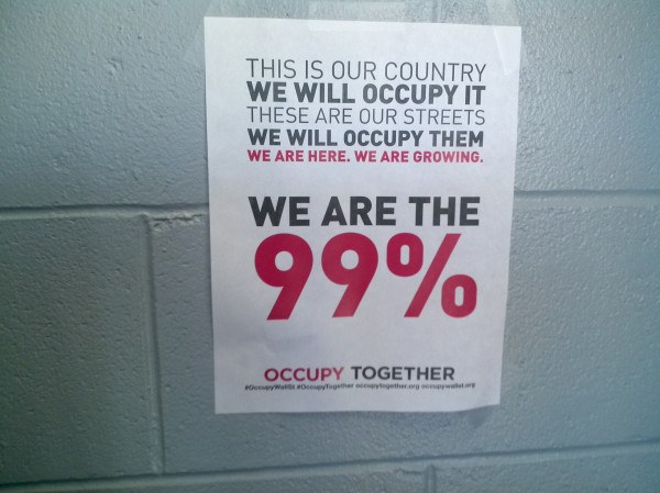 Schwarzes Plakat an einer Wand mit fetter, schwarzer Schrift, die "Occupy Wall Street" und "Wir sind die 99%." lautet.